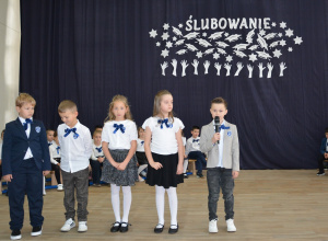 Czworo uczniów w galowych strojach na tle dekoracji