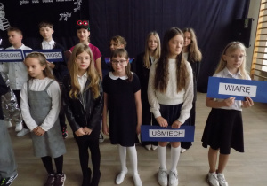 Grup dzieci trzymających w ręku tabliczki, na których zapisane są wartości, np. cierpliwość