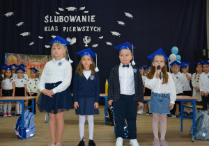 Cztery dziewczynki w galowych strojach na tle granatowej dekoracji