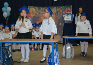 Dzieci stoją prezd szkolnymi ławkami