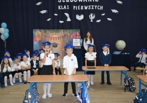 Dzieci stoją prezd szkolnymi ławkami