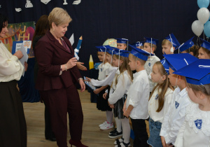 Kobieta z dużym ołówkiem w ręku stoi przed dziećmi