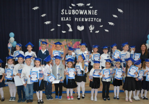 Zdjęcie grupowe dzieci ubranych w galowe stroje na tle granatowego tła