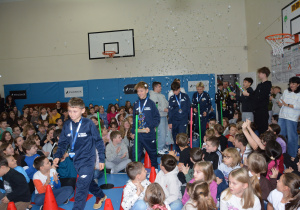 Chłopcy ubrani w granatowe, sportowe stroje wchodzą na salę gimnastyczną, starsi chłopcy otwierają knfetti