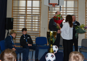 Kobieta w białej bluzce wręcza kwiaty mężczyznom