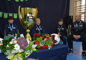 w centrum puchar w kolorze złotym, w tle chłopcy w sportowych strojach