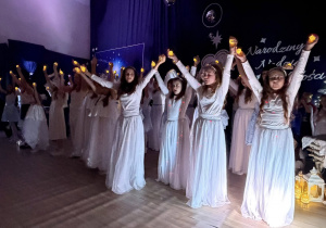 Aktorzy w białych strojach tańczą ze światełkami