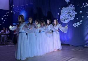 Dziewczynki w białych sukniach z niebieską wstążką tańczą z lampionami