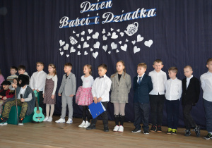 Grupa dzieci w przebraniach i galowych strojach na kle granatowej kotary