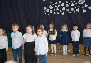 Dzieci w strojach galowych, na tle granatowej kotary