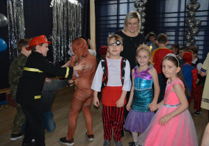 Dzieci w przebraniach pozują do zdjęcia, z tyłu nauczycielka