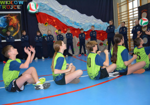 Chłopcy w strojach sportowych siedzą na podłodze, podbijają piłki.